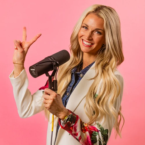 Ashley Wisroth Holding a Microphone Holding Up Peace Sign Pink Background